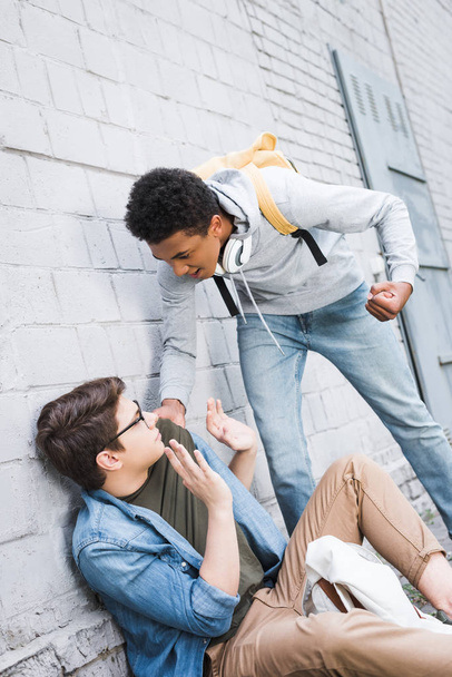 aggressive and brunette african american boy going to punch frightened boy in glasses  - Zdjęcie, obraz