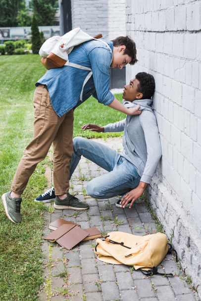 агресивний хлопчик у сорочці знущається над афроамериканським хлопчиком у светрі
  - Фото, зображення
