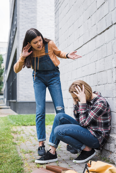 aggressive and brunette teenager bulling blonde and scared teenager - Photo, Image