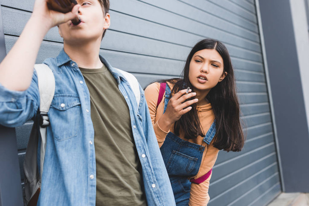 boy and brunette teenager looking away, smoking cigarette and drinking beer  - Foto, Imagen