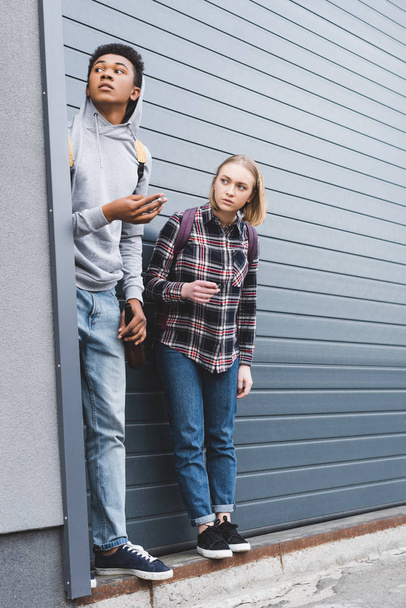 african american boy and blonde teenager looking away, smoking cigarettes and holding beer  - Valokuva, kuva