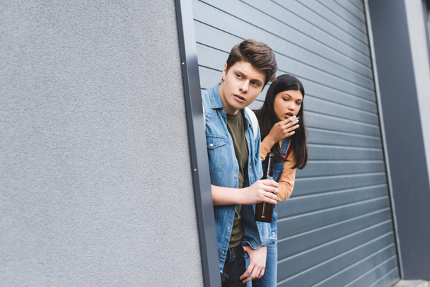 mladík a bruneta, který se dívá jinam, kouří cigaretu a drží pivo  - Fotografie, Obrázek