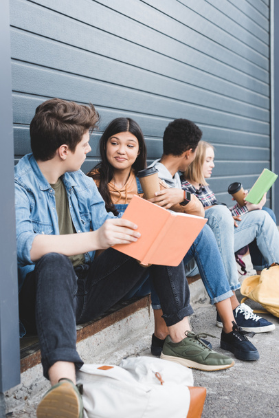 teenagers sitting, talking, holding paper cups and books outside  - Photo, Image