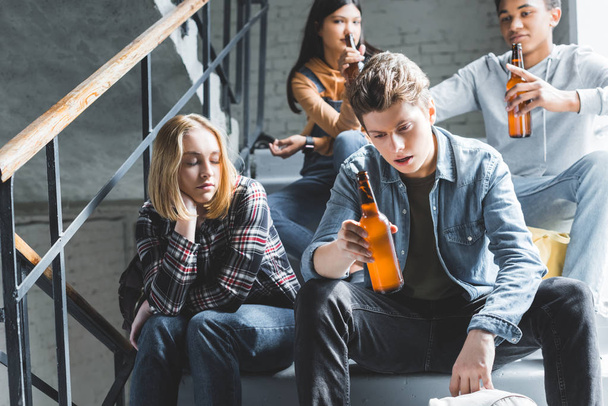 teenagers sitting on stairs, drinking beer from glass bottles and talking  - Photo, Image