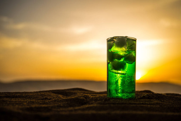 Lähikuva märkä lasi vihreä kylmä minttu juoma, värikäs oranssi auringonlasku tausta terassilla. Jäähdyttävä kesädrinkki. Kesällä raikas ja jäähdytys inspiraatiota, ilta kontrasti väriyhdistelmä
. - Valokuva, kuva