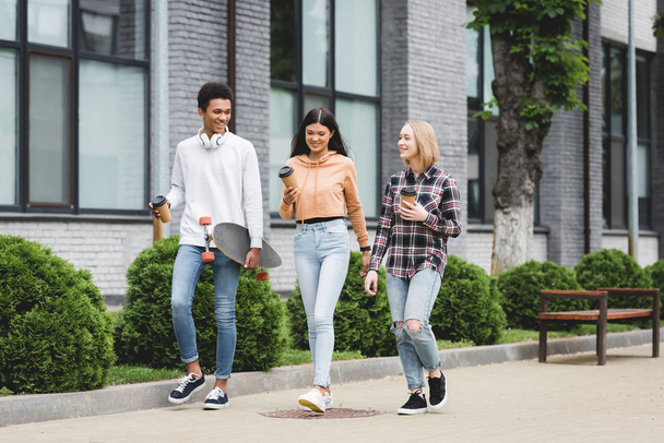 smiling teenagers walking and holding disposable cups and skateboard  - Photo, Image