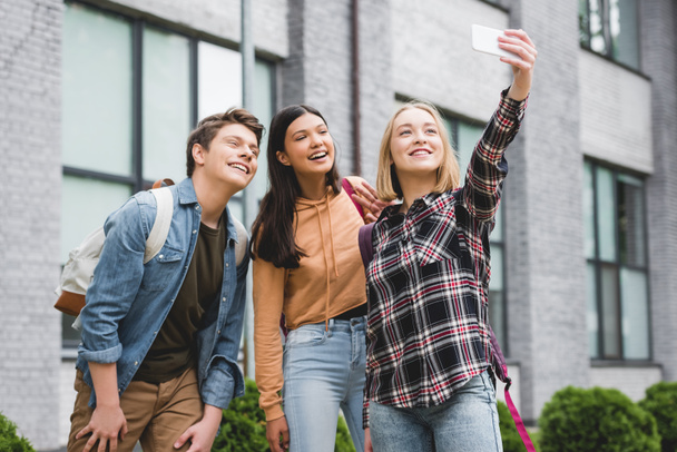 happy teenagers holding smartphone, taking selfie and smiling outside  - Fotografie, Obrázek