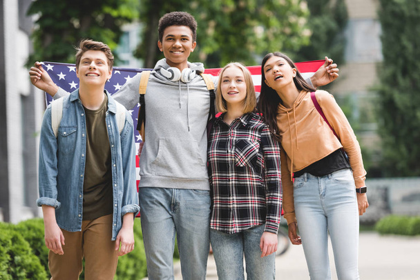 szczęśliwych nastolatków posiadających amerykańską flagę, uśmiechając się i patrząc z dala - Zdjęcie, obraz