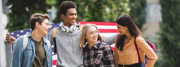 panoramic shot of teenagers holding american flag and talking  - 写真・画像