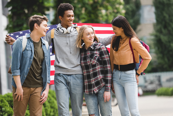 счастливые и улыбающиеся подростки, держащие американский флаг и разговаривающие
  - Фото, изображение