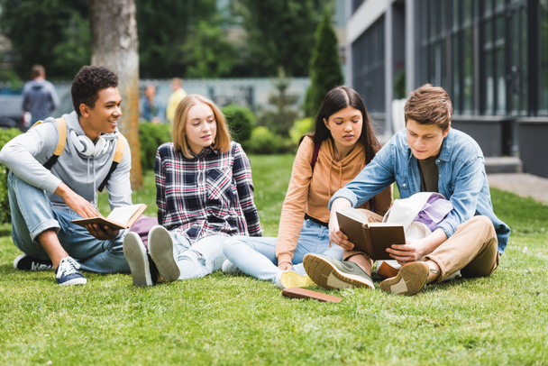 smiling teenagers sitting on grass and reading book outside - Foto, Imagem