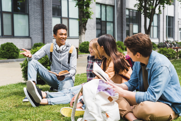 lachende tieners zittend op gras, praten en het houden van boeken  - Foto, afbeelding