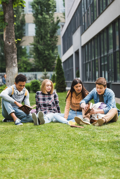 lachende tieners zittend op gras en het lezen van boeken buiten - Foto, afbeelding