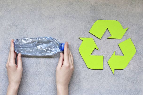 Manos de mujer sosteniendo botella de plástico con símbolo de reciclaje sobre fondo gris
. - Foto, imagen