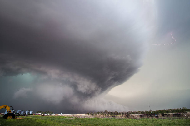 Une énorme tempête supercellulaire avec un nuage de mur de grattage au sol remplit le ciel au-dessus des terres agricoles du Nebraska. Les grèves peuvent être observées dans son énorme courant ascendant rotatif
. - Photo, image