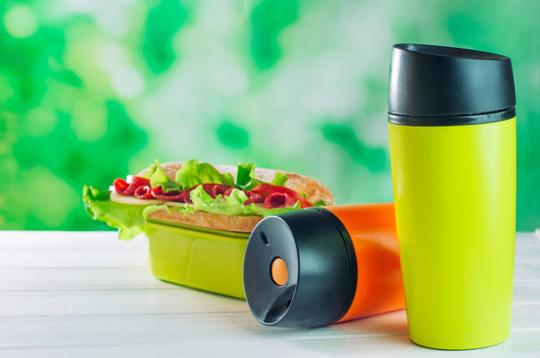 Color thermos mugs near lunch box on the white wooden table - Photo, Image