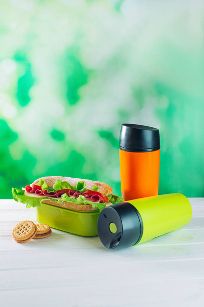Кольорові термос чашки біля обідньої коробки над світло-зеленим боке фоном
 - Фото, зображення