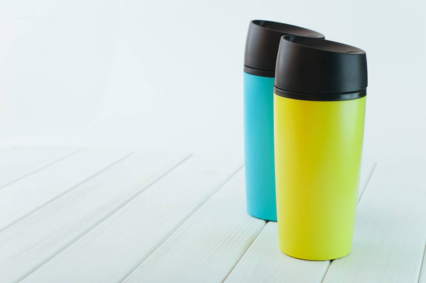 Color thermos mugs on the white wooden table - Foto, Imagem
