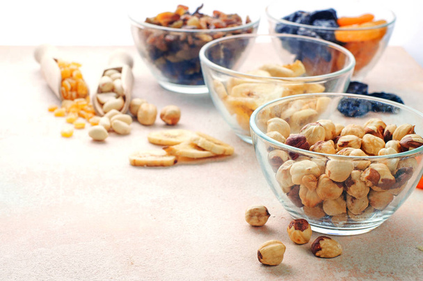 Сушеные фрукты, орехи и семена в мисках на светло-бежевом фоне - Фото, изображение