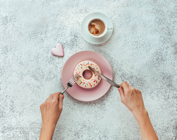 Female hands with fork and knife cutting donut shape biscuit - Fotografie, Obrázek