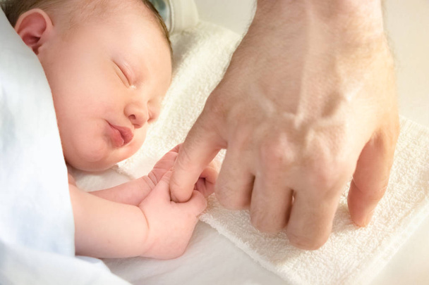 Baby sleeping holding the finger of his father. - Фото, зображення