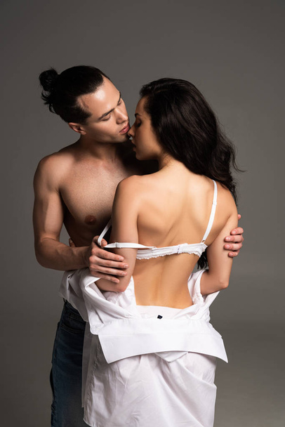 shirtless jonge man omarmen met sexy vriendin geïsoleerd op grijs - Foto, afbeelding