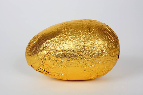 Huevo de Pascua de chocolate envuelto en lámina de oro sobre un fondo blanco
. - Foto, Imagen