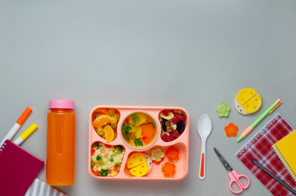 Boîte à lunch avec jus d'orange et cahiers sur fond gris - Photo, image