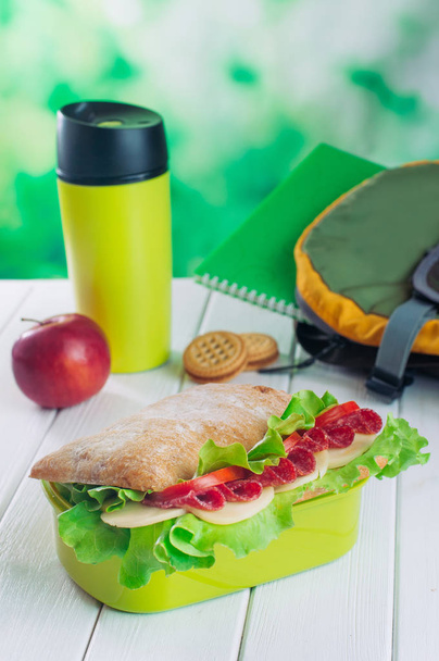 Caja de almuerzo con sándwich cerca de la jarra de thermos y mochila escolar. - Foto, Imagen