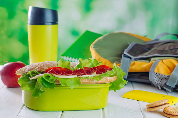 Caja de almuerzo con sándwich cerca de la jarra de thermos, manzana, galletas, backp. - Foto, Imagen