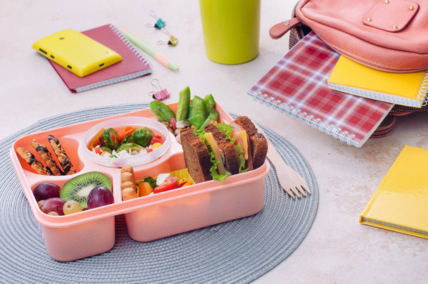 Обеденная коробка с бутербродами, салатом, свежими фруктами и орехами - Фото, изображение
