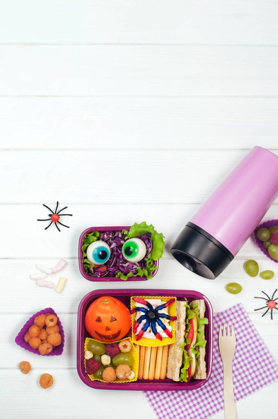 Open Halloween lunch box with school lunch near thermo mug on wh - Foto, imagen