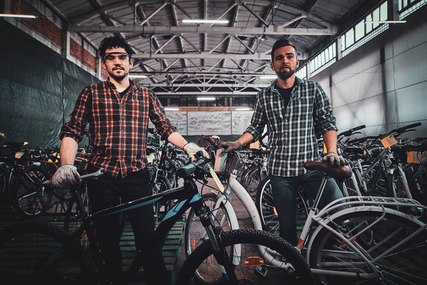 Δύο άντρες με ποδήλατα ποζάρουν για φωτογράφο στην αποθήκη. - Φωτογραφία, εικόνα