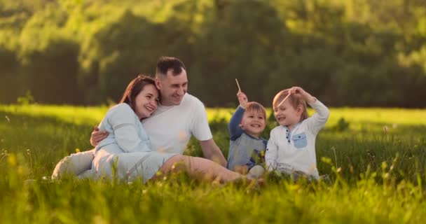 Papà mamma e due figli in estate al tramonto seduti in un prato sull'erba ridendo e abbracciandosi
 - Filmati, video