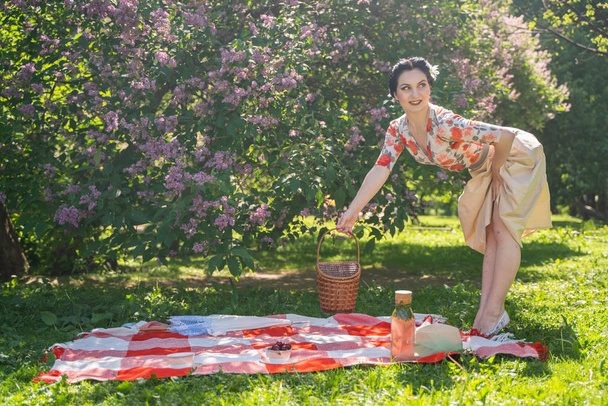 魅力的なブルネットの若い女の子は、一人で緑の夏の草の上に休息とピクニックを楽しんでいます。かわいい女性は休日を持っており、自然に空き地を過ごす. - 写真・画像
