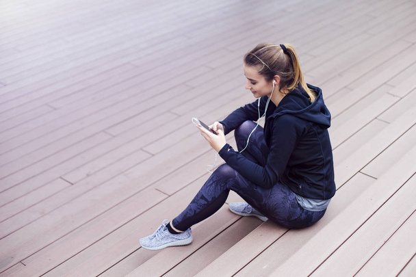 Mladá sportovní žena pomocí mobilu a posezení na schodech venku - Fotografie, Obrázek