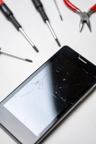 Smartphone with broken and cracked screen with screwdrivers and pliers on white background. Vertical. - Photo, Image