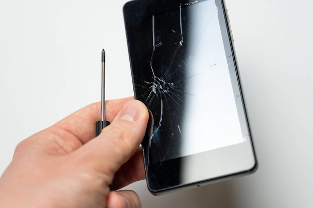 Smartphone with broken screen and screwdriver in mens hand in front of white background. - Foto, Bild