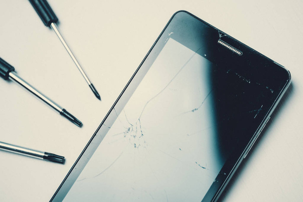 Smartphone met gebroken en gebarsten scherm met schroevendraaiers op witte achtergrond. Afgezwakt. - Foto, afbeelding