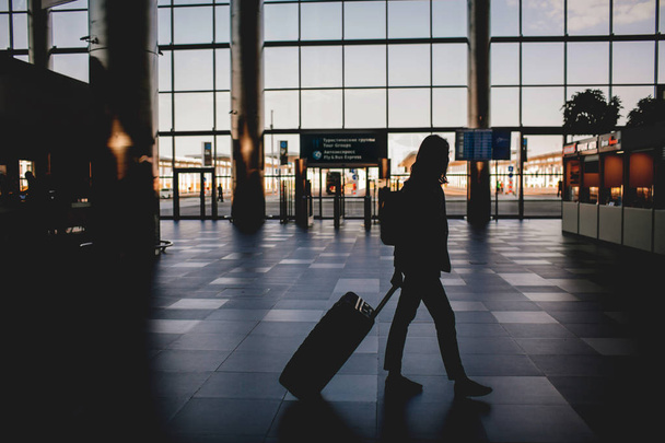 Silhouette of a girl at the airport with suitcase and backpack. - Foto, afbeelding