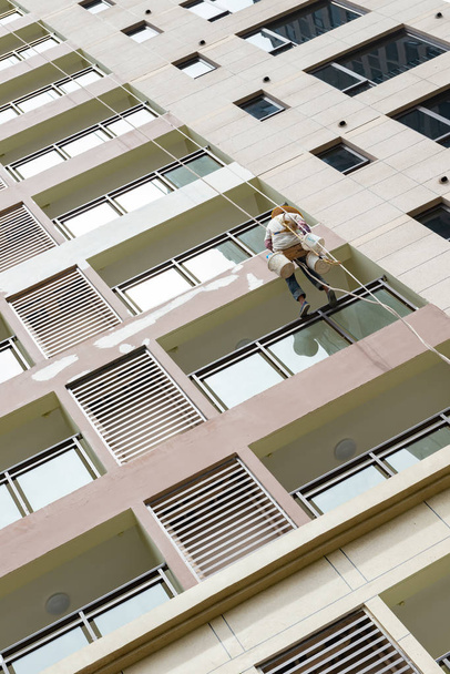 worker hanging with ropes and painting the oustside of a highrise building - Photo, Image
