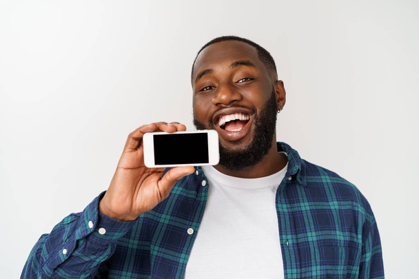 Przystojny afrykański facet odizolowany na szarym tle, prezentując inteligentny telefon i wskazując palcem na pustym czarnym ekranie. - Zdjęcie, obraz
