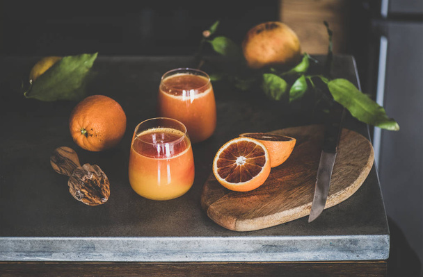 Two glasses of freshly squeezed blood orange juice or smoothie and fresh fruits on concrete kitchen counter. Healthy lifestyle, vegan, vegetarian, alkaline diet, spring detox concept - Fotoğraf, Görsel