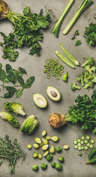 Healthy vegan ingredients layout. Flat-lay of whole and cut green vegetables and herbs over concrete background, top view, narrow composition. Vegetarian, weight loss, raw, clean eating concept - Foto, Imagen