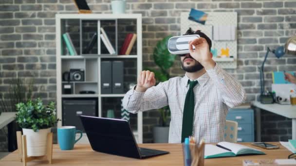 Young man using virtual reality glasses at work wearing headset gesturing - Πλάνα, βίντεο