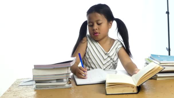 Linda niña asiática pensando y escribiendo en cuaderno sobre fondo blanco
, - Metraje, vídeo