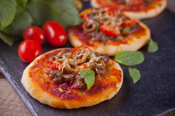 Mini pizza fatta in casa sul piatto nero
 - Foto, immagini