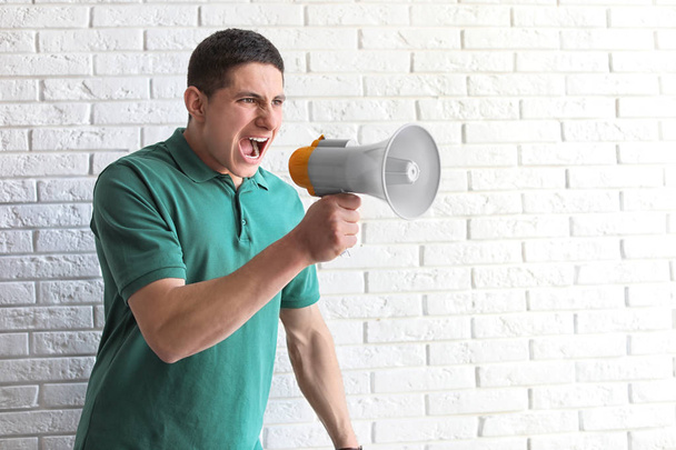 Portrait of young man using megaphone near brick wall. Space for text - Fotoğraf, Görsel