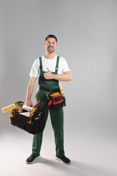 Full length portrait of professional construction worker with tools on grey background - Fotó, kép