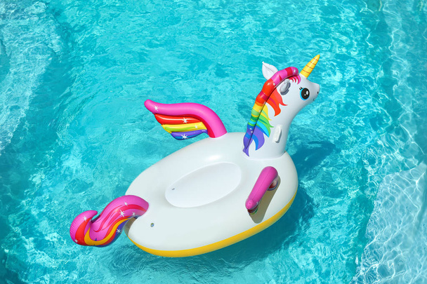 Funny inflatable unicorn ring floating in swimming pool on sunny day - Fotoğraf, Görsel